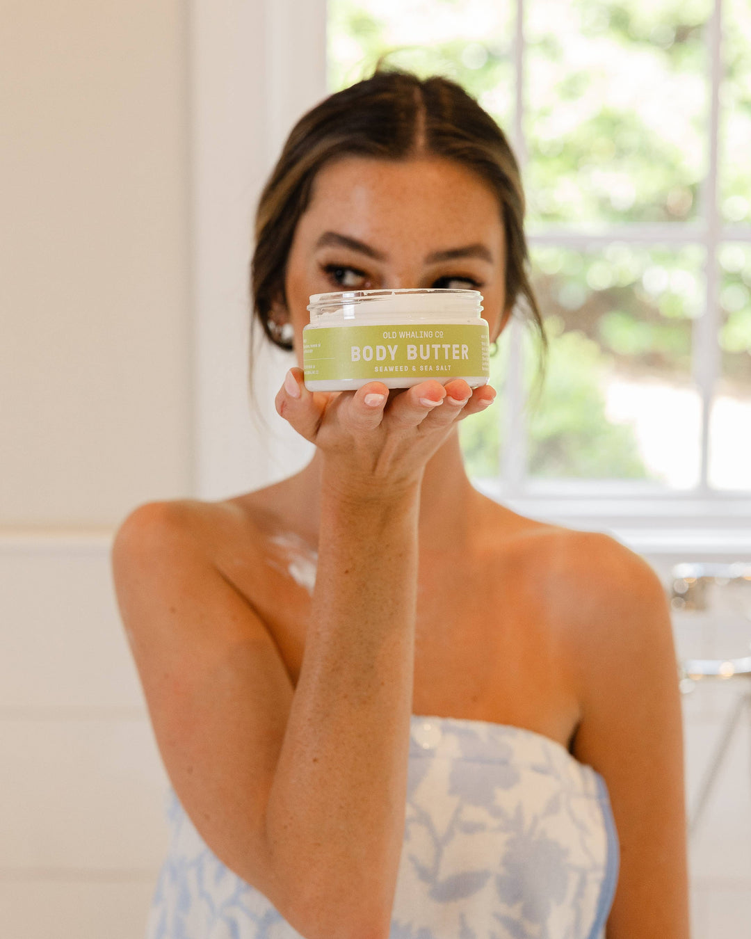 Woman holding a jar of body butter in a bathroom setting