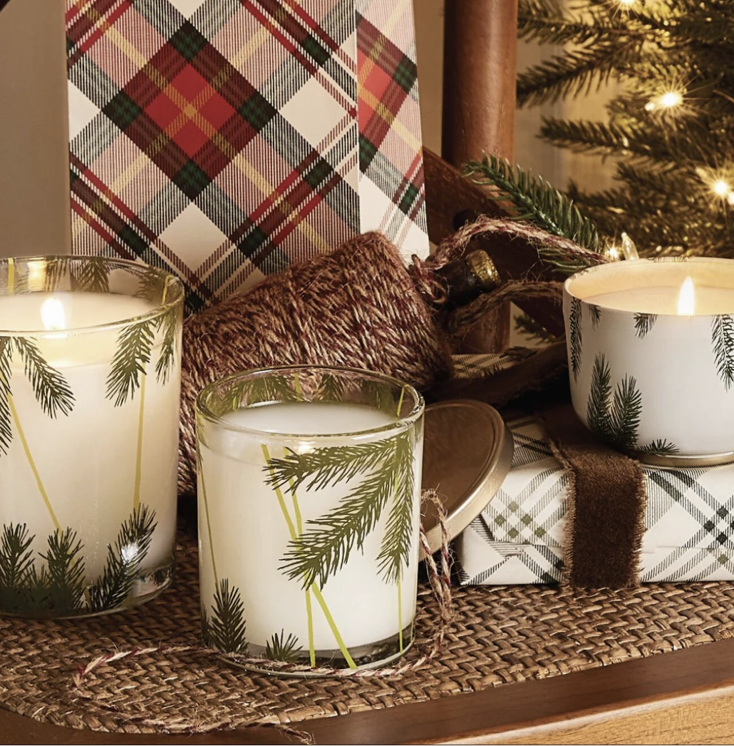 Candles with pine tree design on a decorative table setting with plaid fabric and Christmas tree.