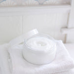 White jar of cream on a white towel with a light blue patterned background