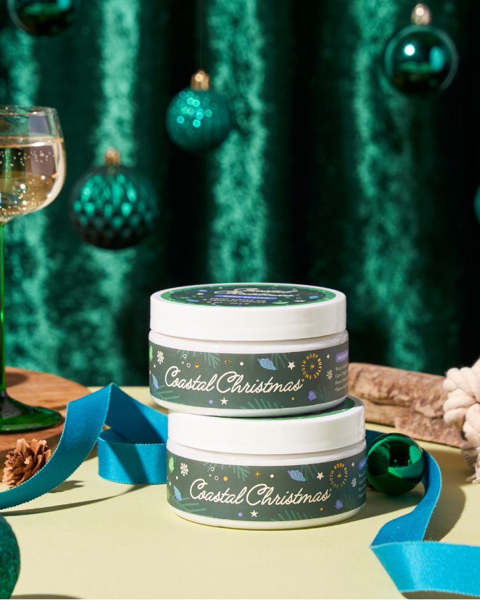 Two jars labeled 'Coastal Christmas' on a table with festive decorations including ornaments and a glass of champagne.