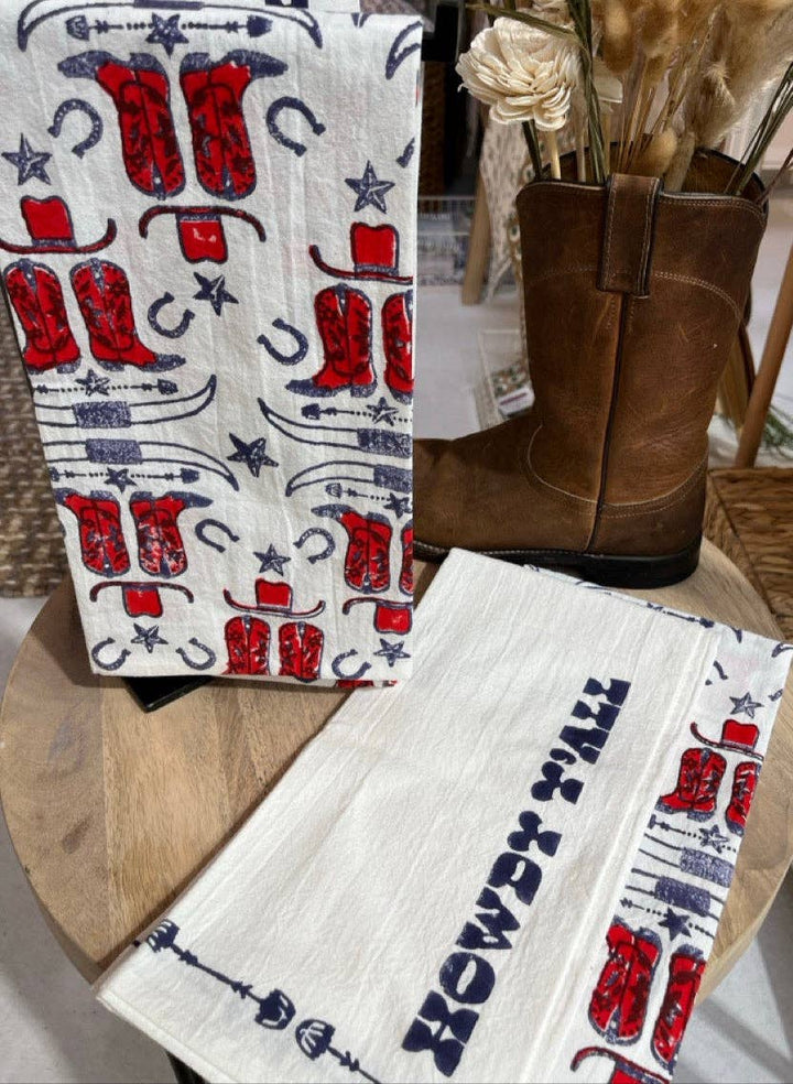 Towel with cowboy boot design on a wooden surface next to a brown boot.