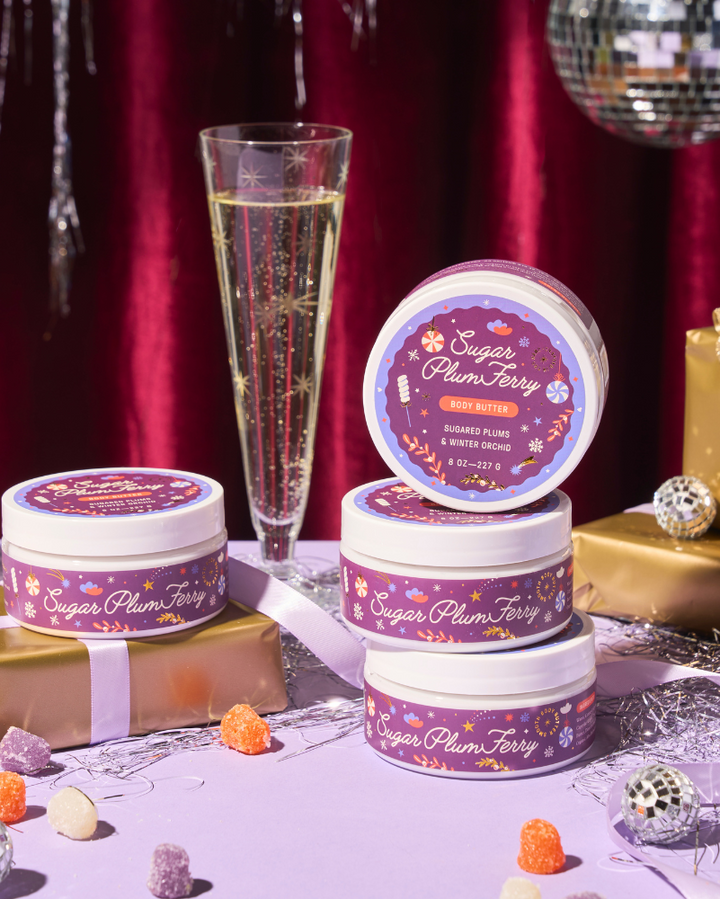 Decorative tins labeled 'Sugar Plum Fairy' with a glass of champagne and gift boxes on a festive background.