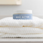 Body butter container on a folded towel on a marble surface