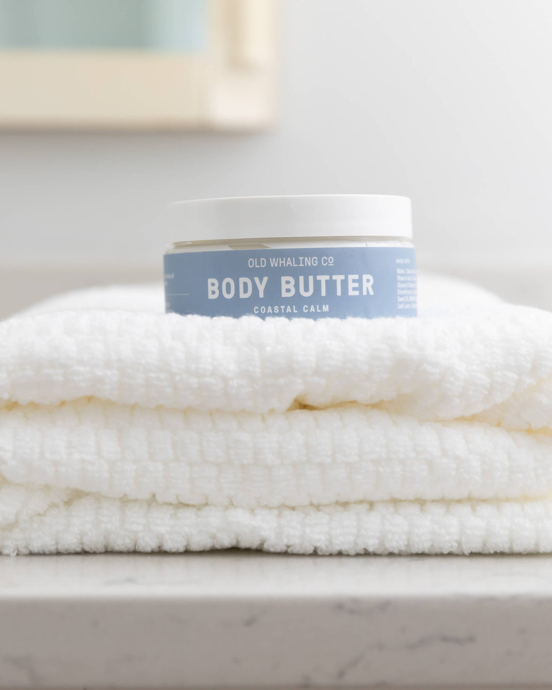 Body butter container on a folded towel on a marble surface