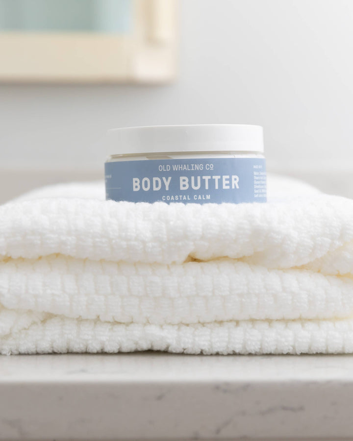 Body butter container on a folded towel on a marble surface