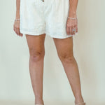 A woman modeling a sleeveless deep magenta top and white shorts against a plain cream studio background.