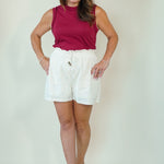 A woman modeling a sleeveless magenta top and white drawstring shorts against a plain light beige studio background.