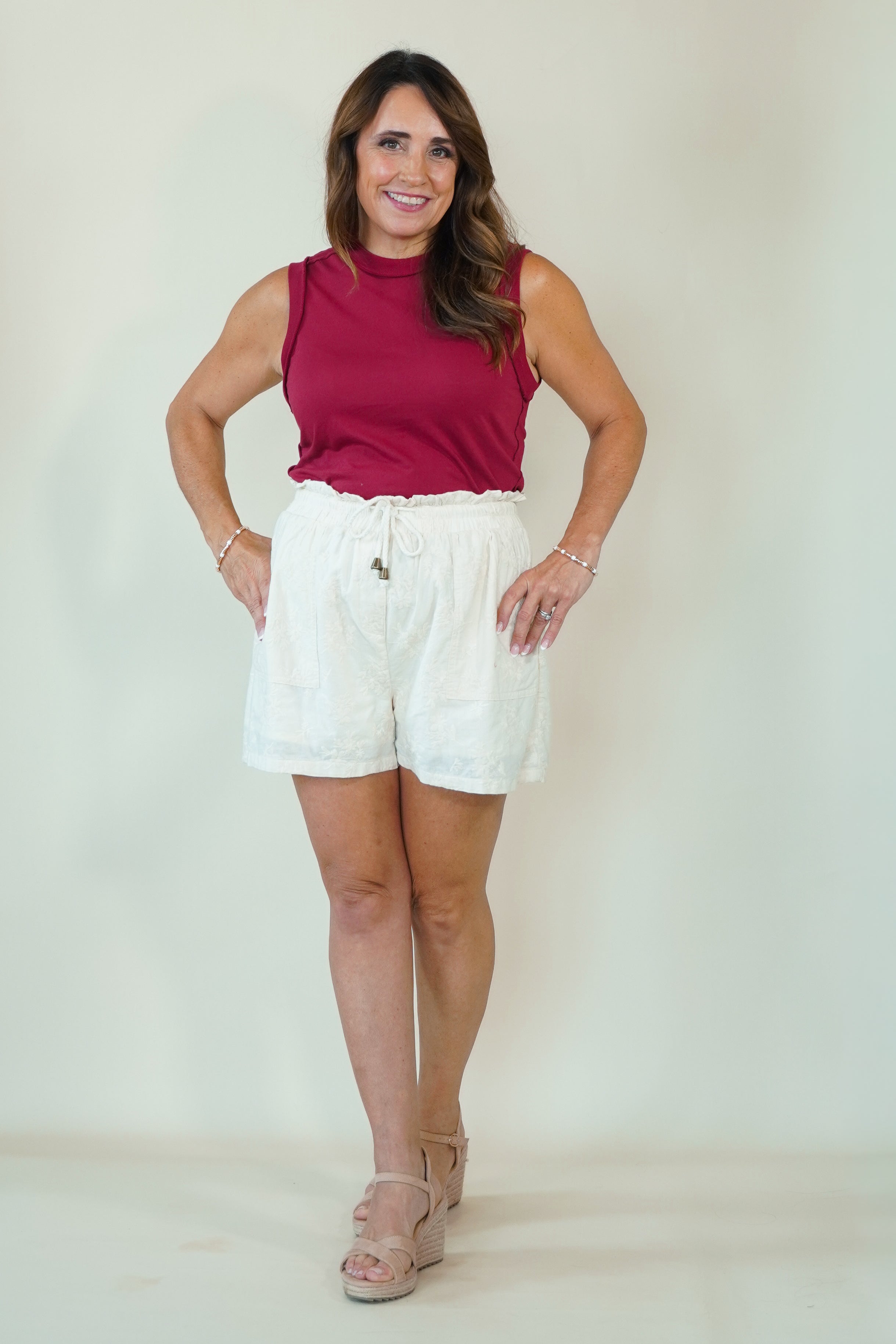 A woman modeling a sleeveless magenta top and white drawstring shorts against a plain light beige studio background.