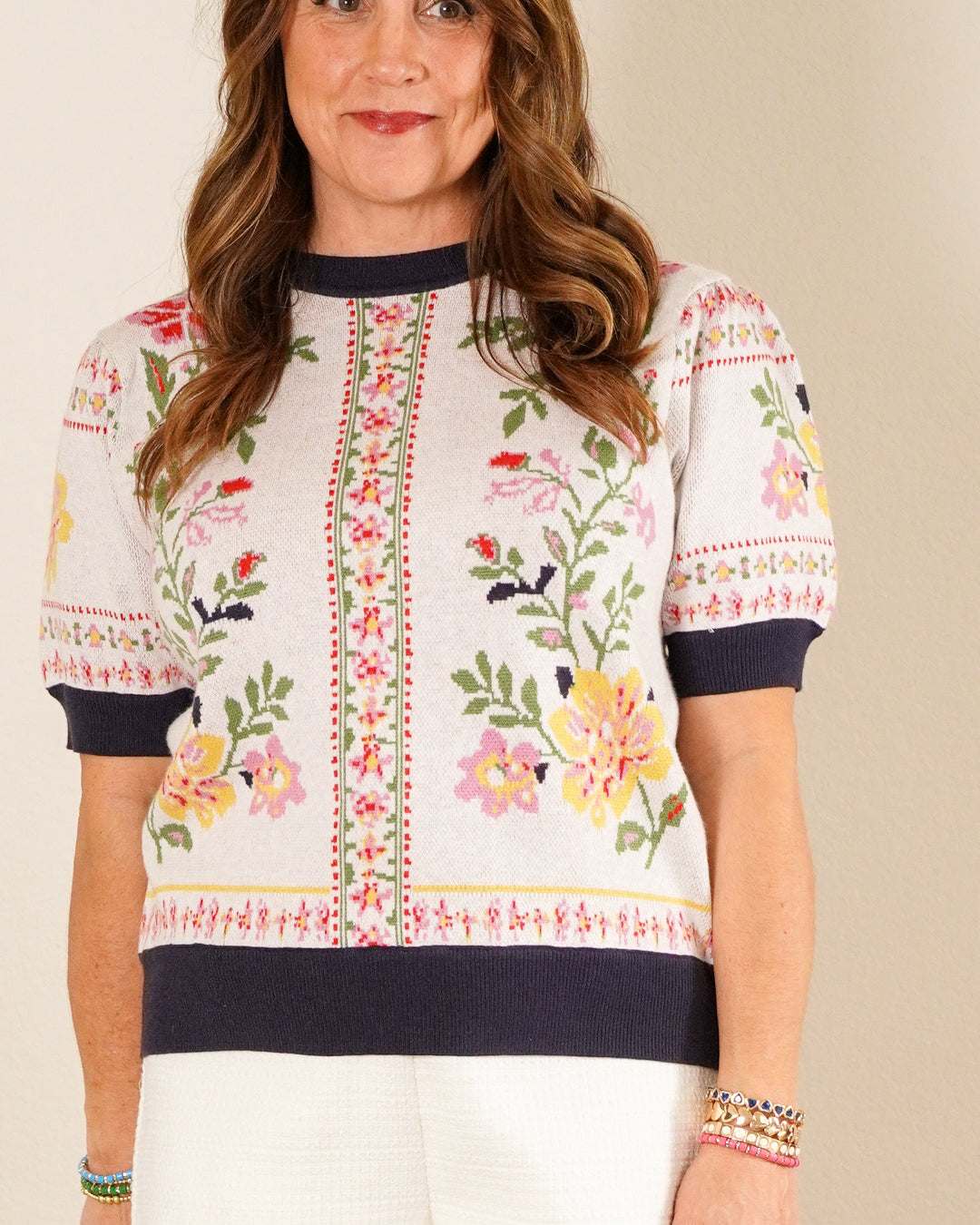 Woman wearing a floral embroidered top and white shorts against a plain background