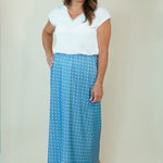 A woman modeling a white short-sleeve top and a blue maxi skirt with a white polka dot pattern, standing against a plain beige studio background.