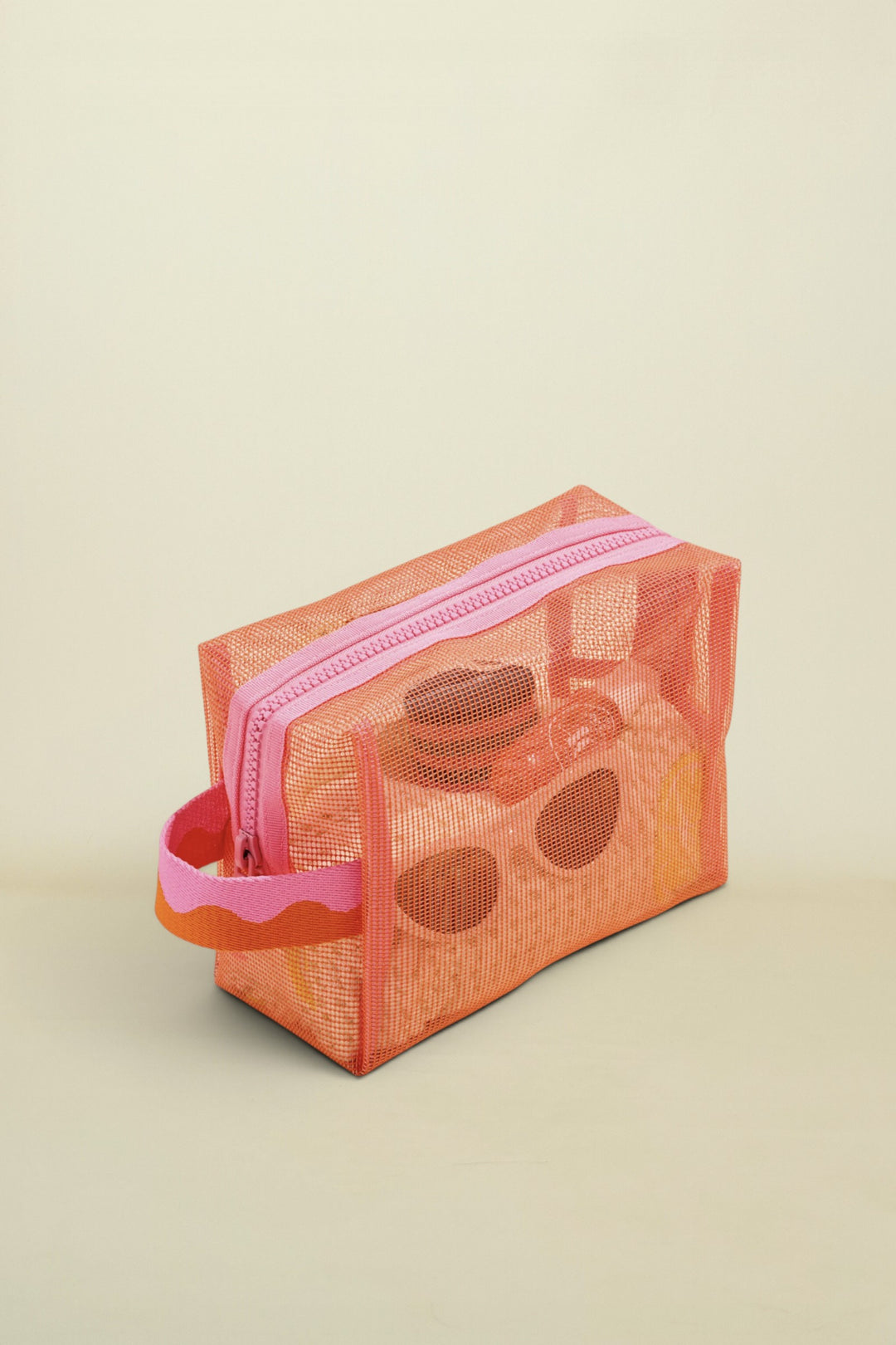 Mesh toiletry bag with pink zipper on a beige background