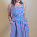 Woman in a blue dress standing in front of a mirror with a light source above.