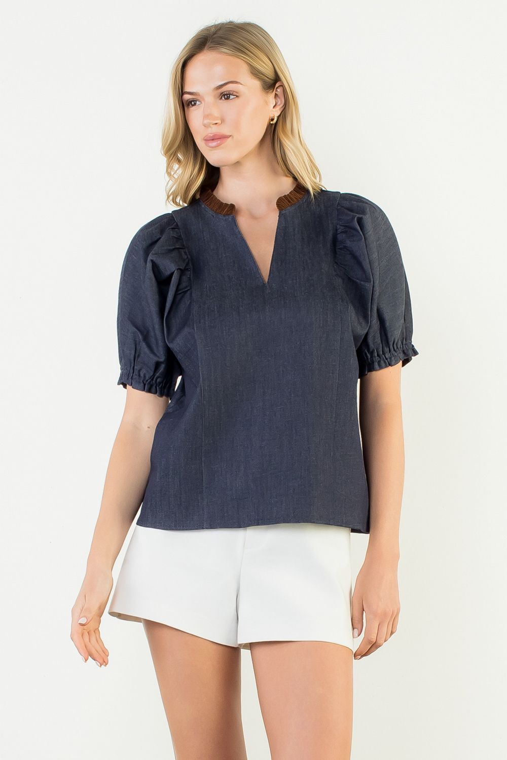 Woman wearing a navy blue blouse with puff sleeves and white shorts on a white background