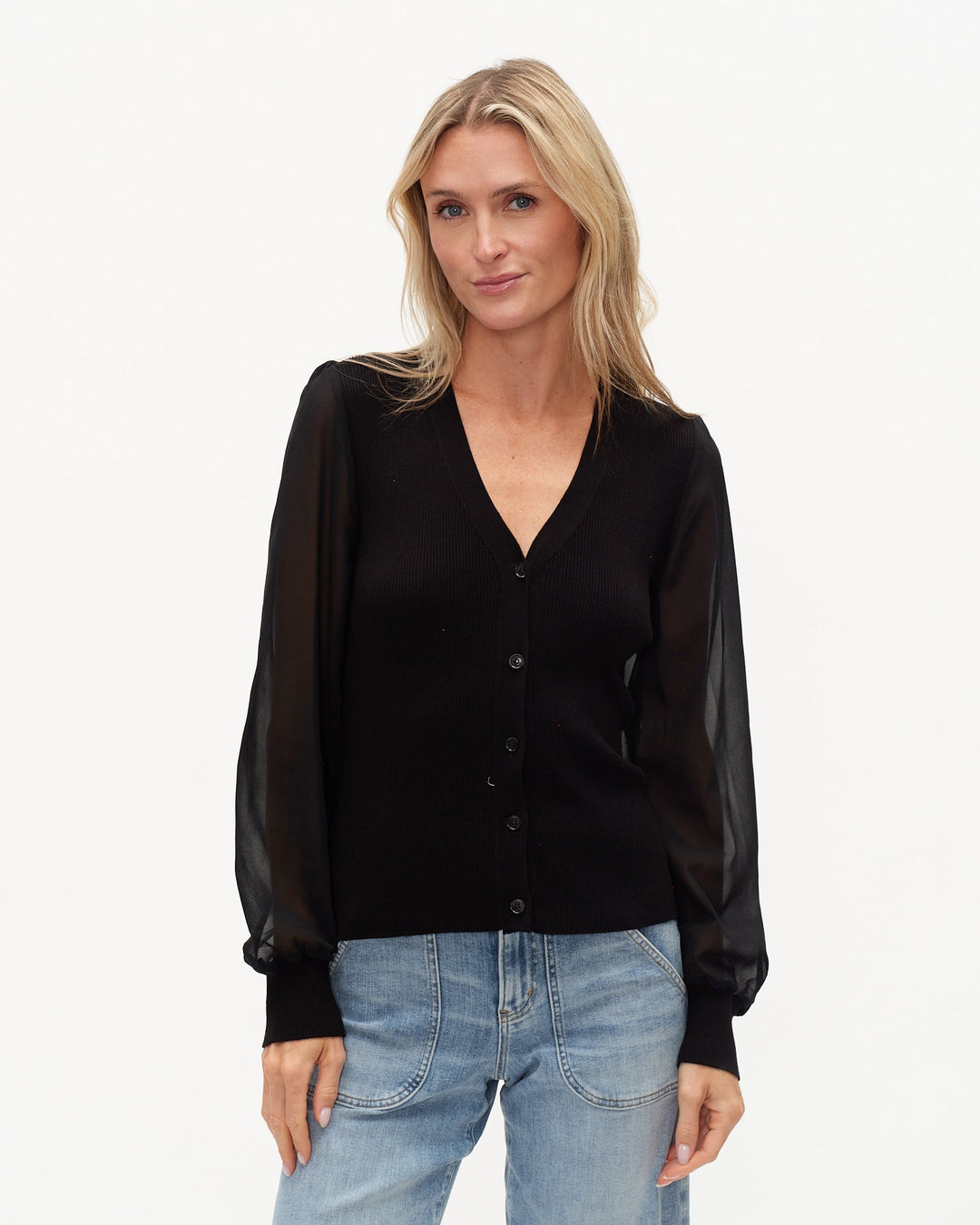Woman wearing a black blouse with sheer sleeves and light blue jeans on a white background