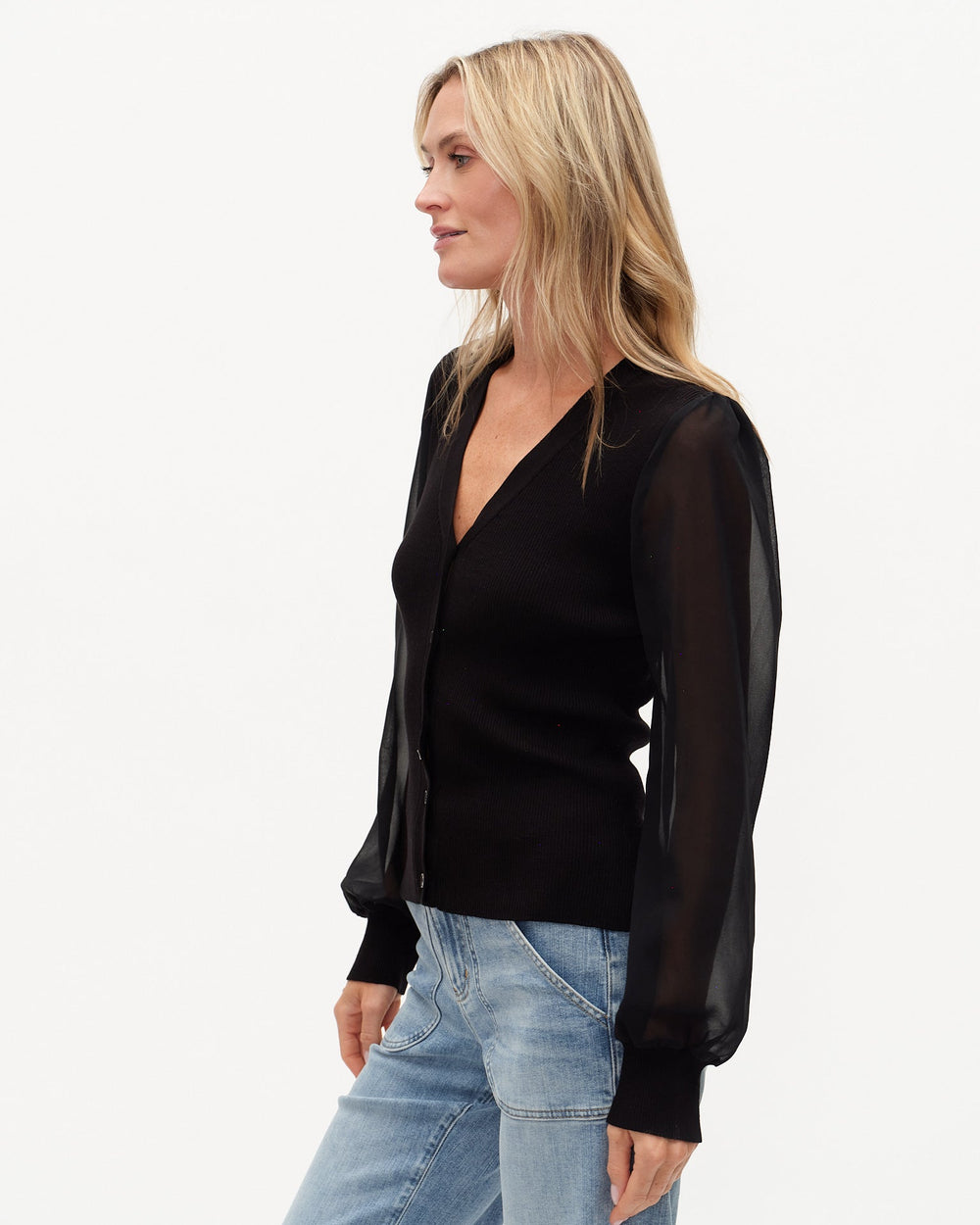 Woman wearing a black blouse with sheer sleeves and light blue jeans on a white background