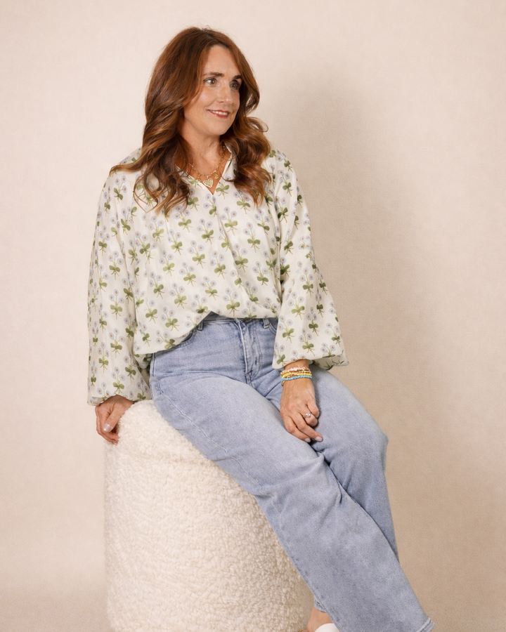Woman sitting on a white cushion wearing a floral blouse and blue jeans against a beige background