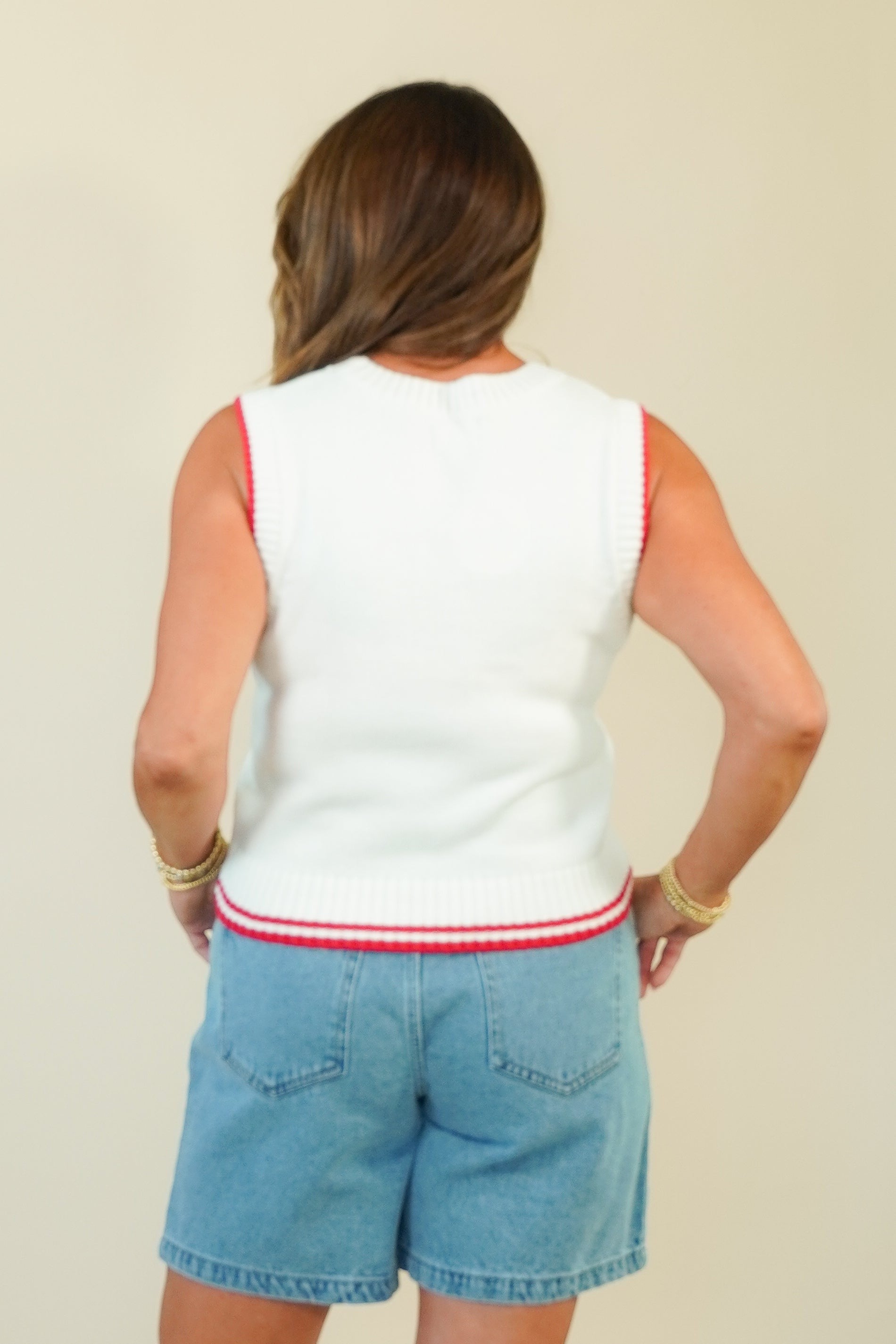 A woman shown from the back wearing a white sleeveless knit top with red trim and light blue denim shorts against a plain beige background.