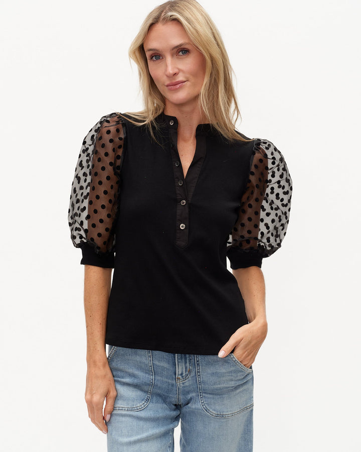 Woman wearing a black blouse with sheer sleeves featuring polka dot patterns on a white background
