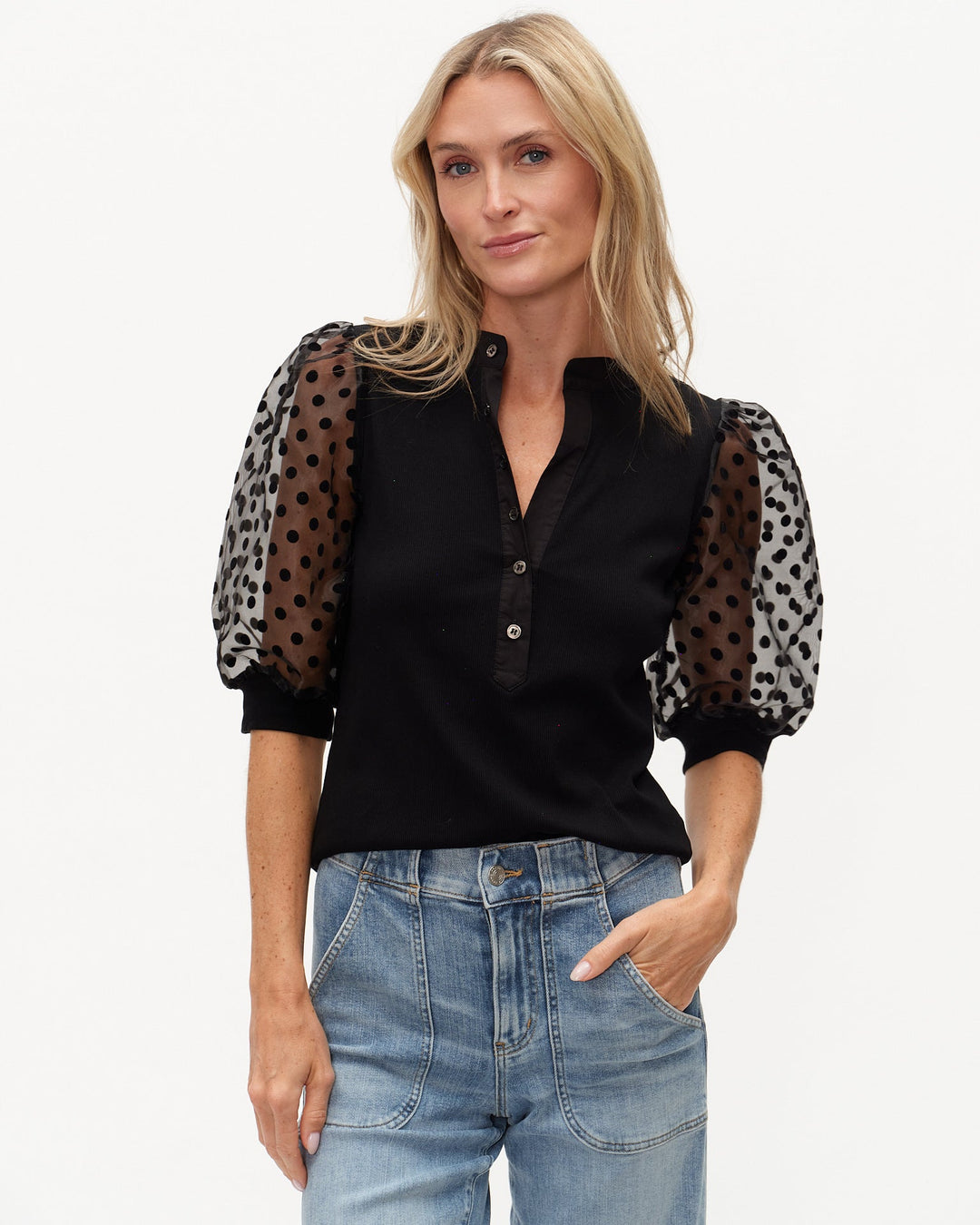 Woman wearing a black blouse with sheer sleeves featuring animal print patterns, paired with blue jeans.