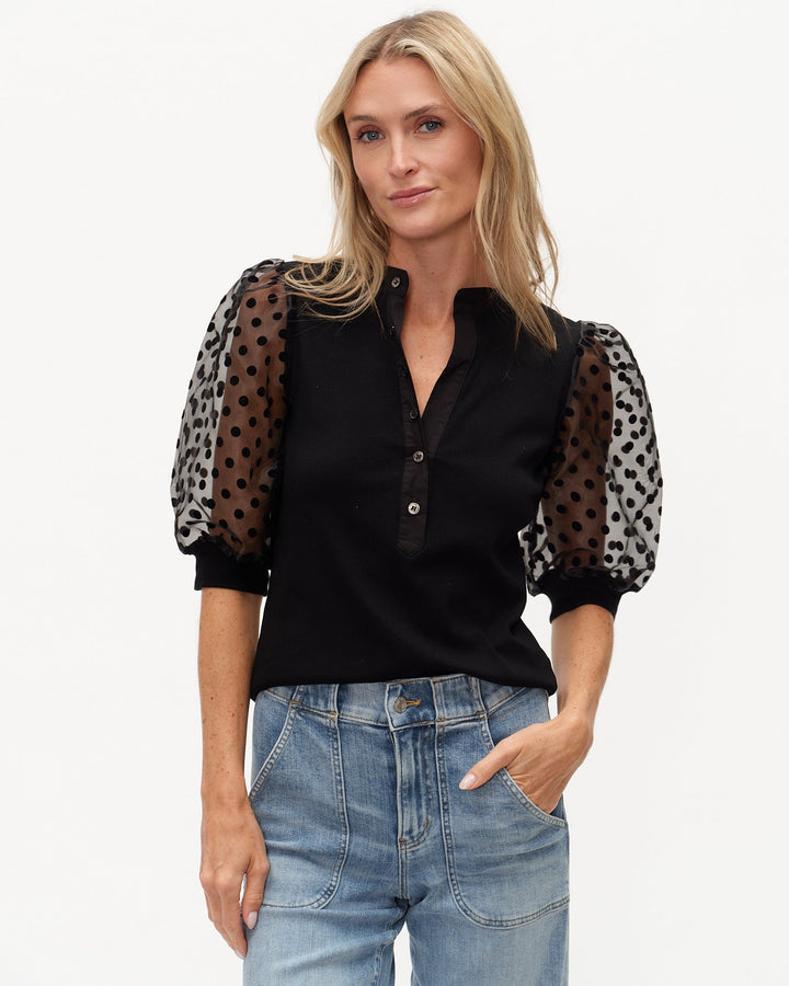 Woman wearing a black blouse with sheer sleeves featuring animal print patterns, paired with blue jeans.