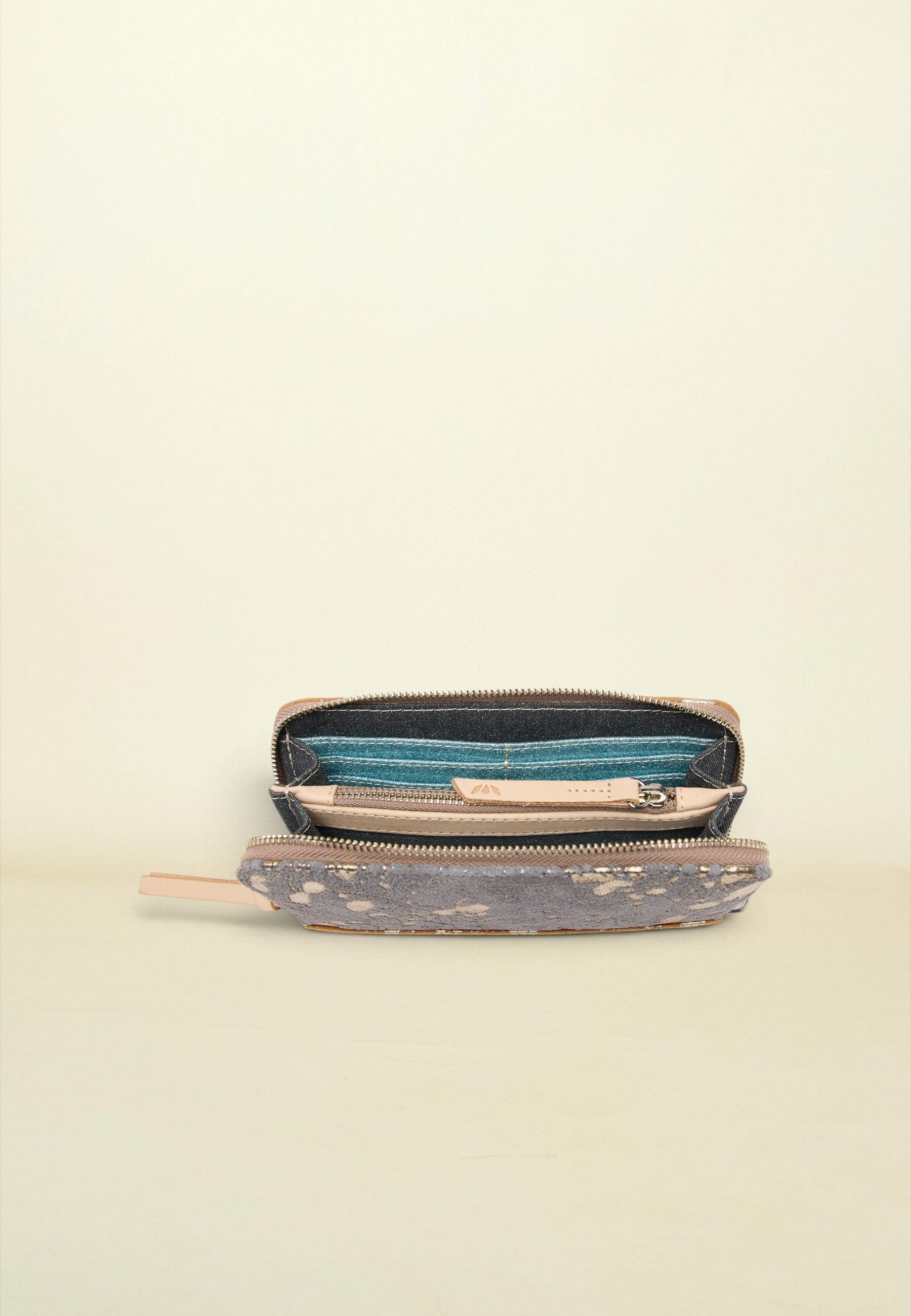 An open zippered pouch or wallet with a distressed gray patterned exterior, a teal blue interior lining, and a light beige interior, shown on a plain cream background.