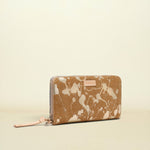 A zip-around wallet with a tan and cream marble pattern, featuring a small pink leather brand tab and a matching pink zipper pull, set against a solid cream background.