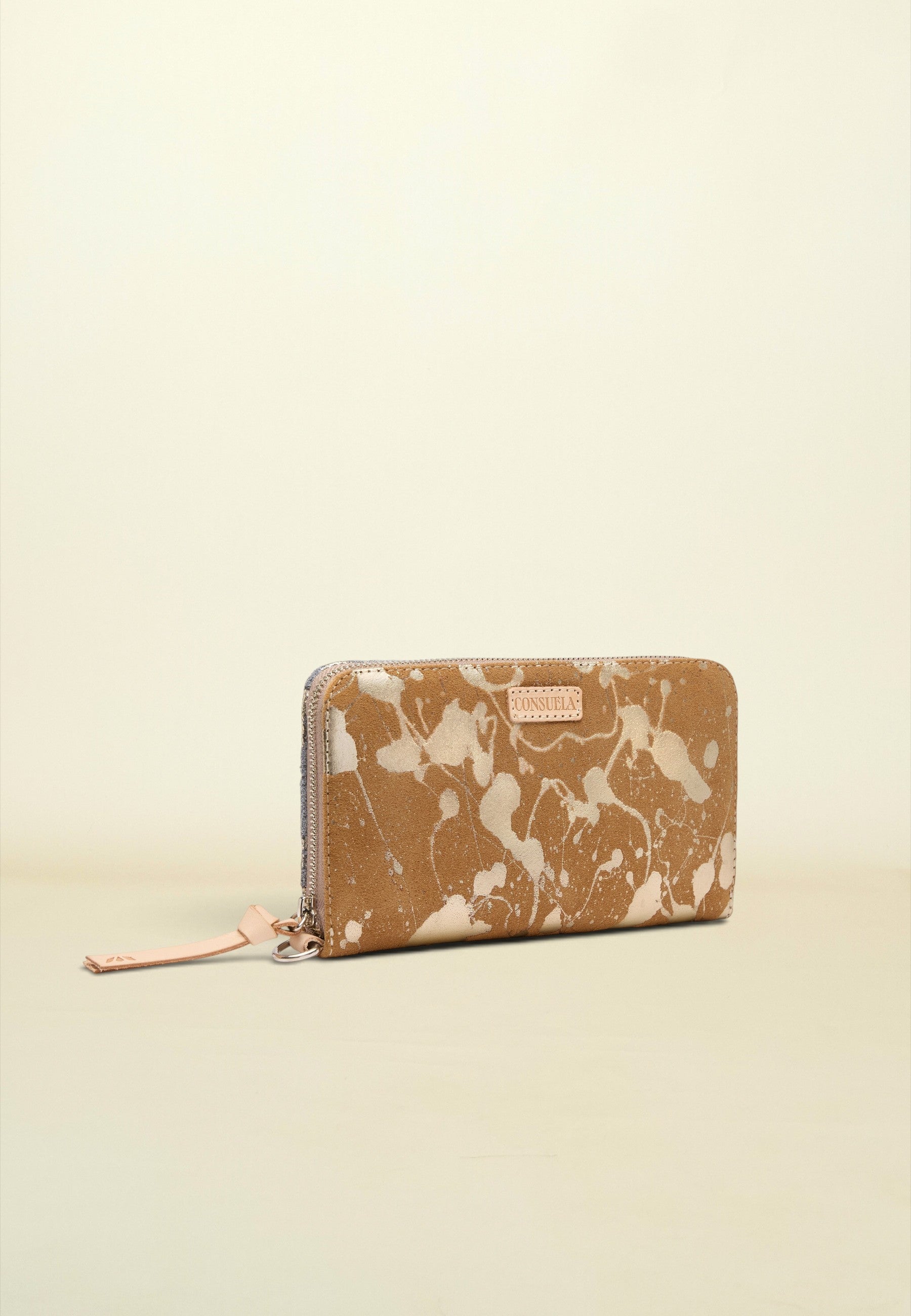 A zip-around wallet with a tan and cream marble pattern, featuring a small pink leather brand tab and a matching pink zipper pull, set against a solid cream background.