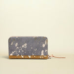 A zip-around wallet with a distressed slate blue and white patterned exterior and a textured gold base, shown on a plain cream background.