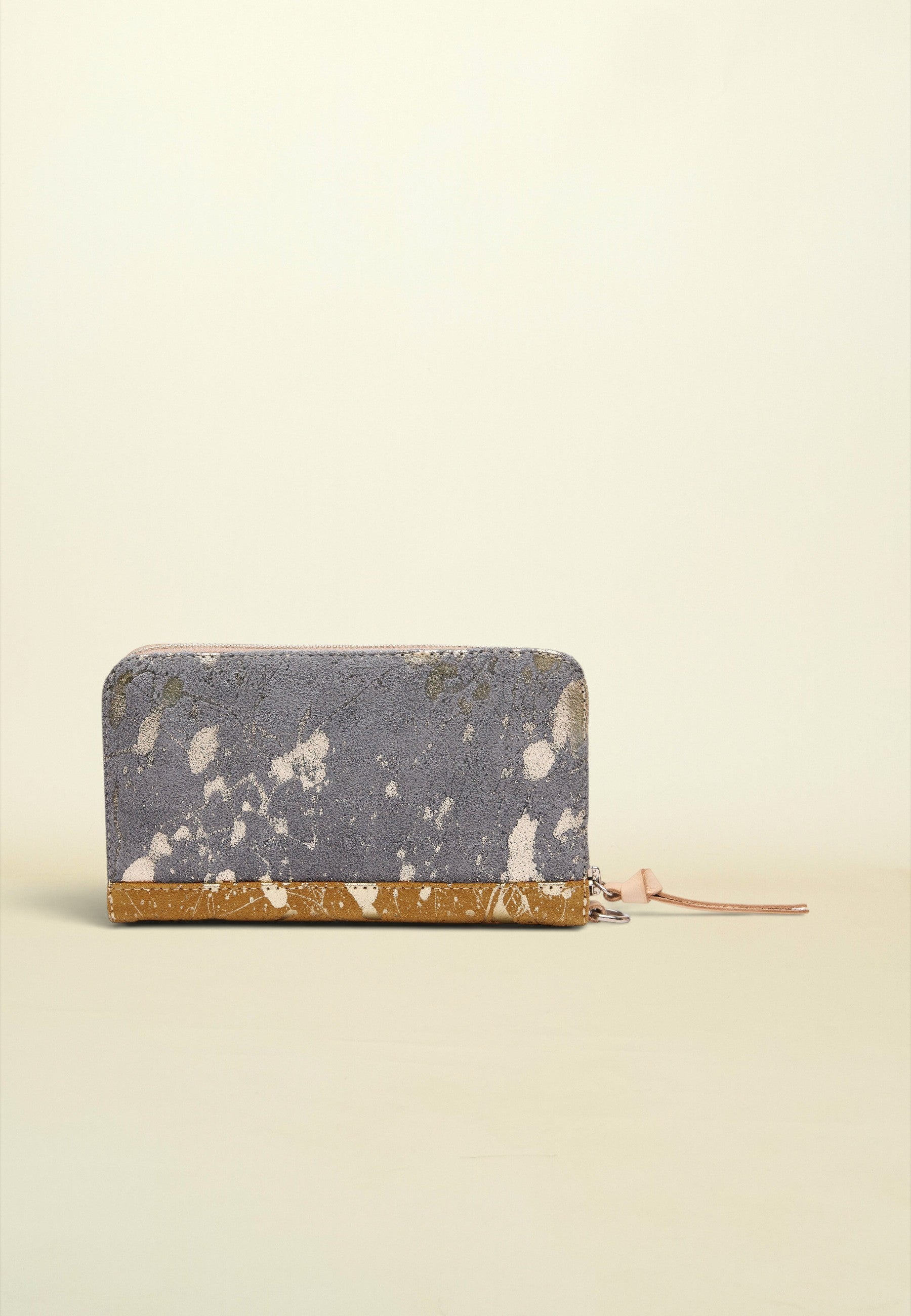 A zip-around wallet with a distressed slate blue and white patterned exterior and a textured gold base, shown on a plain cream background.