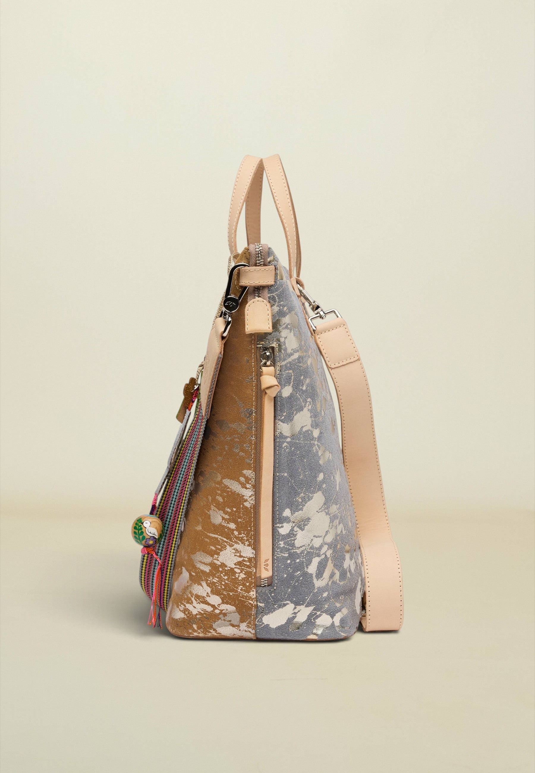 A structured handbag with a split design, featuring a brown and white marbled pattern on one side and a dusty blue and white marbled pattern on the other, with light beige leather handles, a shoulder strap, and zipper pulls, set against a solid light beige background.