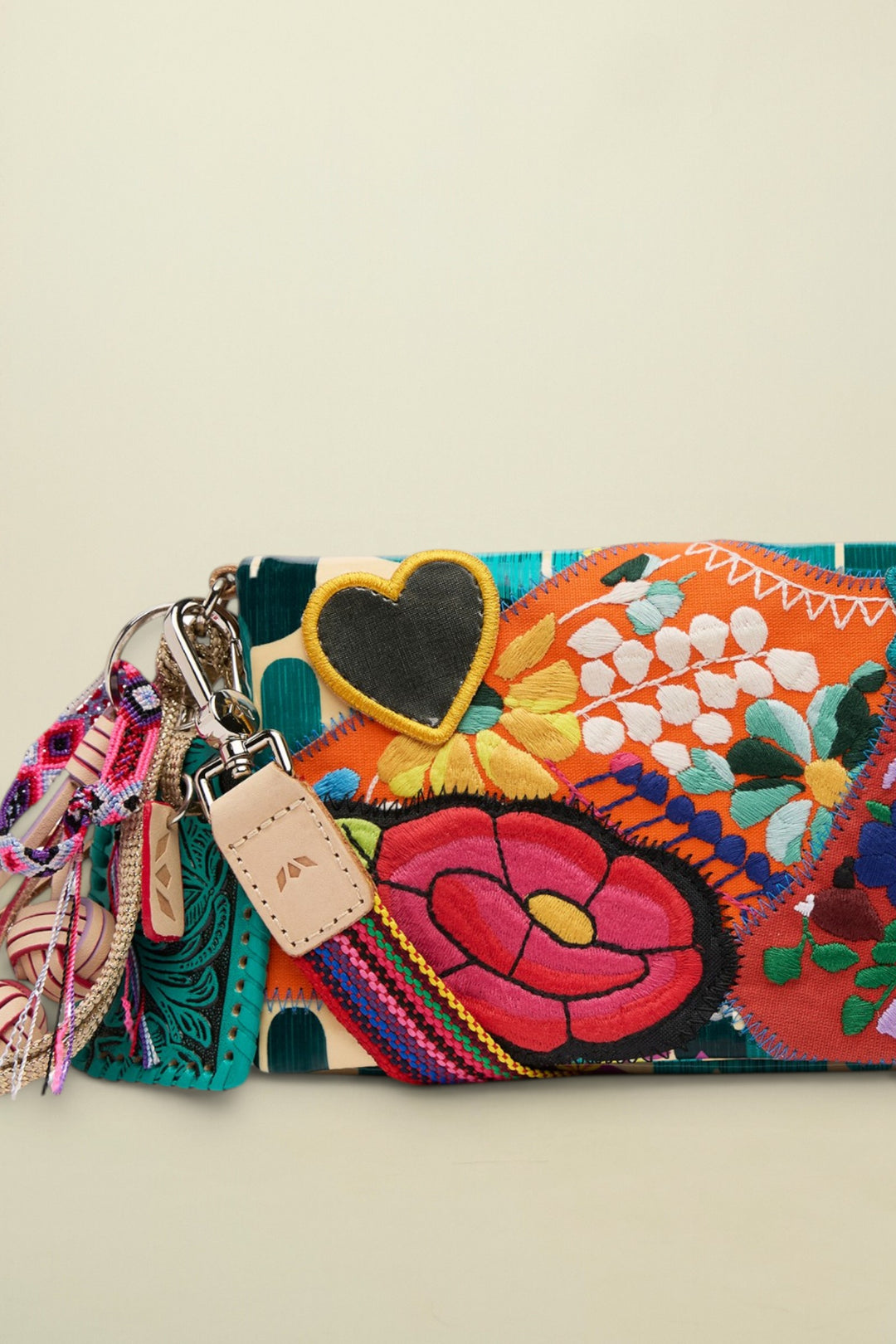 Close up of a colorful embroidered clutch bag with a black heart patch and a leather strap