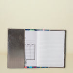 Consuela Gemma Notebook open to a lined page and a schedule page, with a silver textured cover