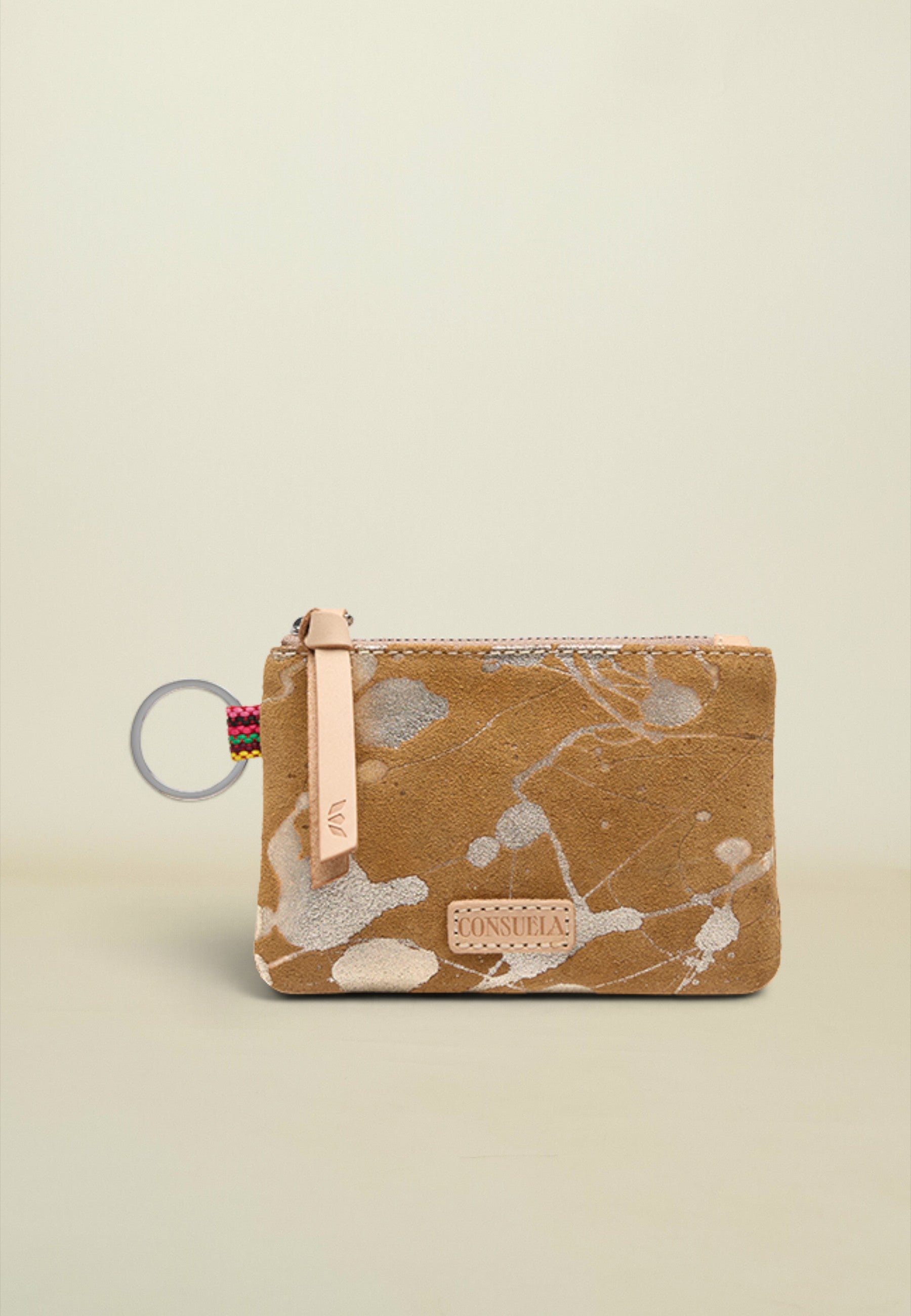 A small zip pouch with a brown and beige abstract paint splatter pattern, featuring a light pink leather zipper pull, a silver metal key ring, and a small rectangular brand patch on the front.