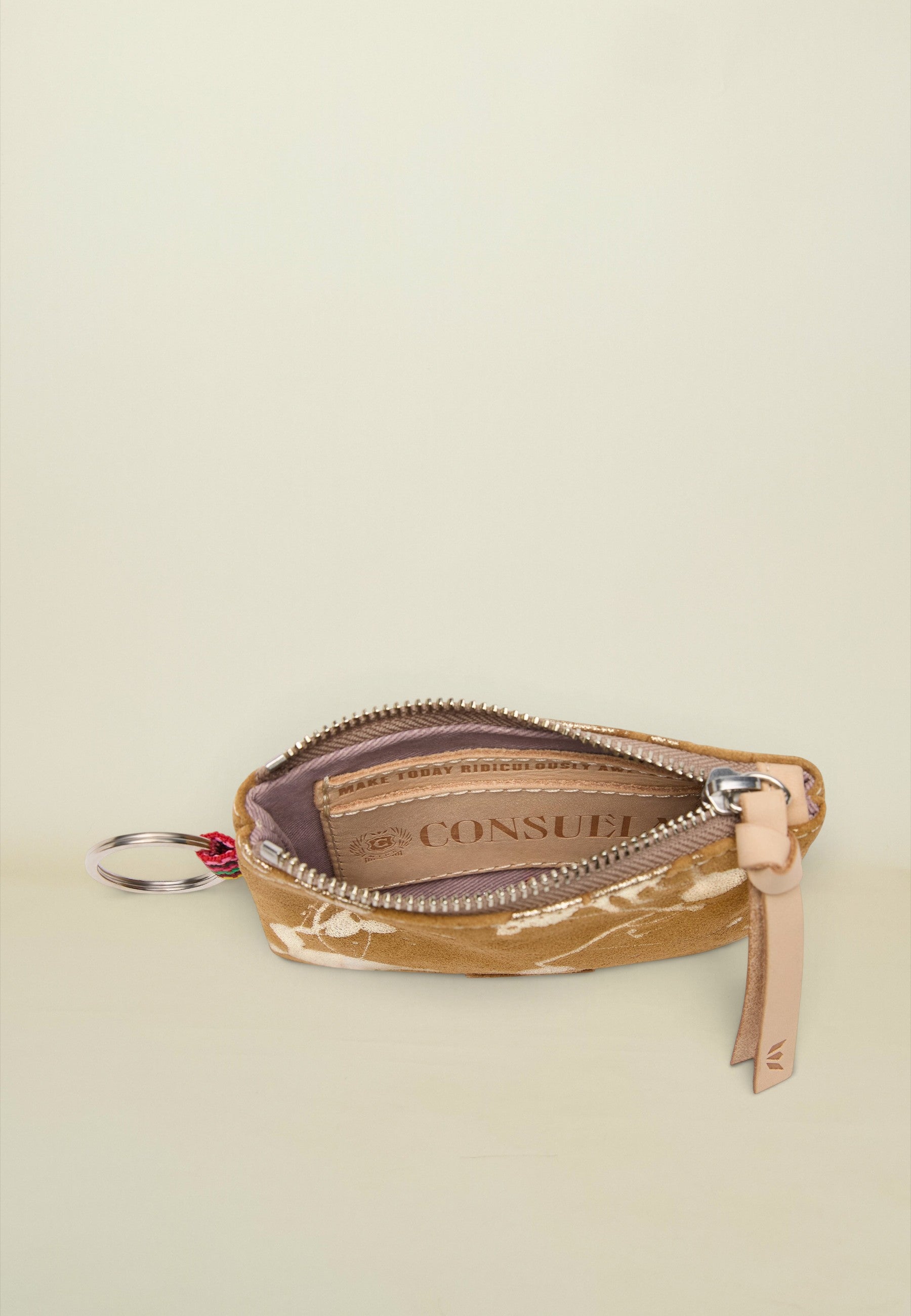 A small zippered pouch with a gold and white marble pattern, featuring a beige leather zipper pull and a silver keyring attachment. The brand name 'CONSUE' is printed on the interior label.