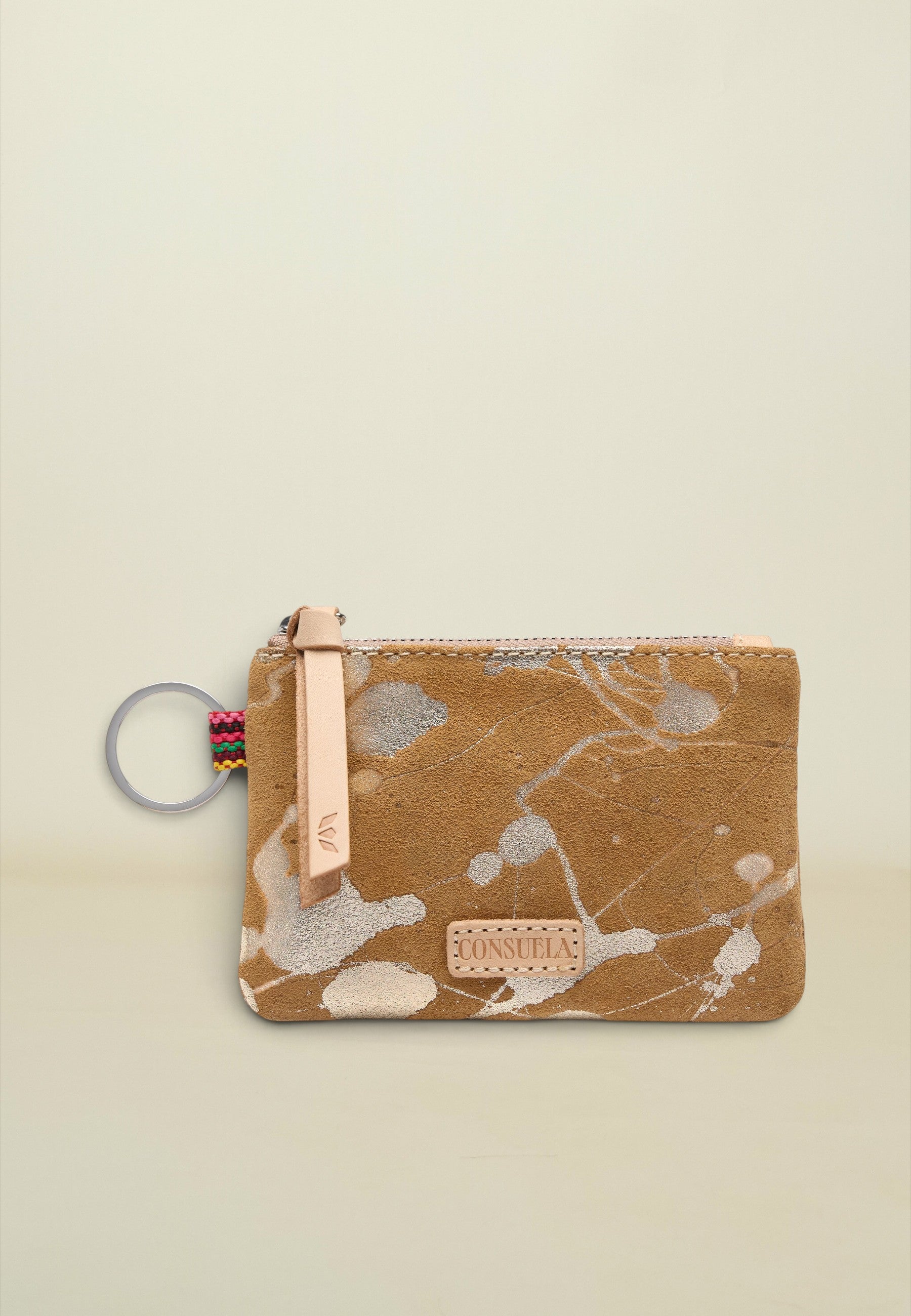 A small zippered pouch with a brown suede-like finish and a white and gray paint splatter pattern. It features a light tan leather zipper pull with the brand name 'CONSIDAS' and a colorful braided key ring attached on the left, set against a solid light beige background.