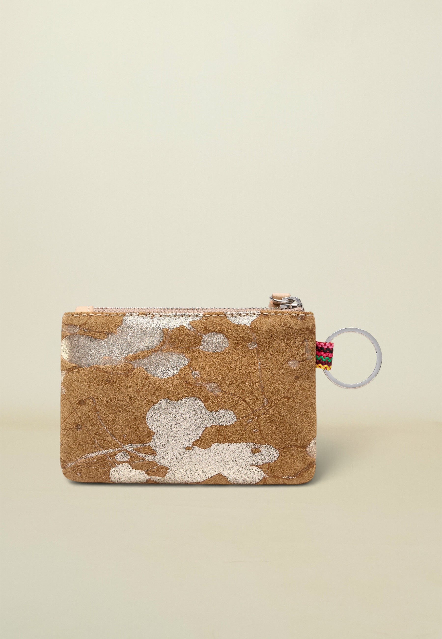 A small zippered pouch with a tan and white cowhide pattern, featuring a silver zipper, a small colorful striped pull tab, and a clear plastic key ring, set against a solid light beige background.