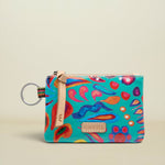 A small zippered pouch with a colorful abstract print on a turquoise background, featuring a beige leather strap and a silver key ring, set against a plain beige background.