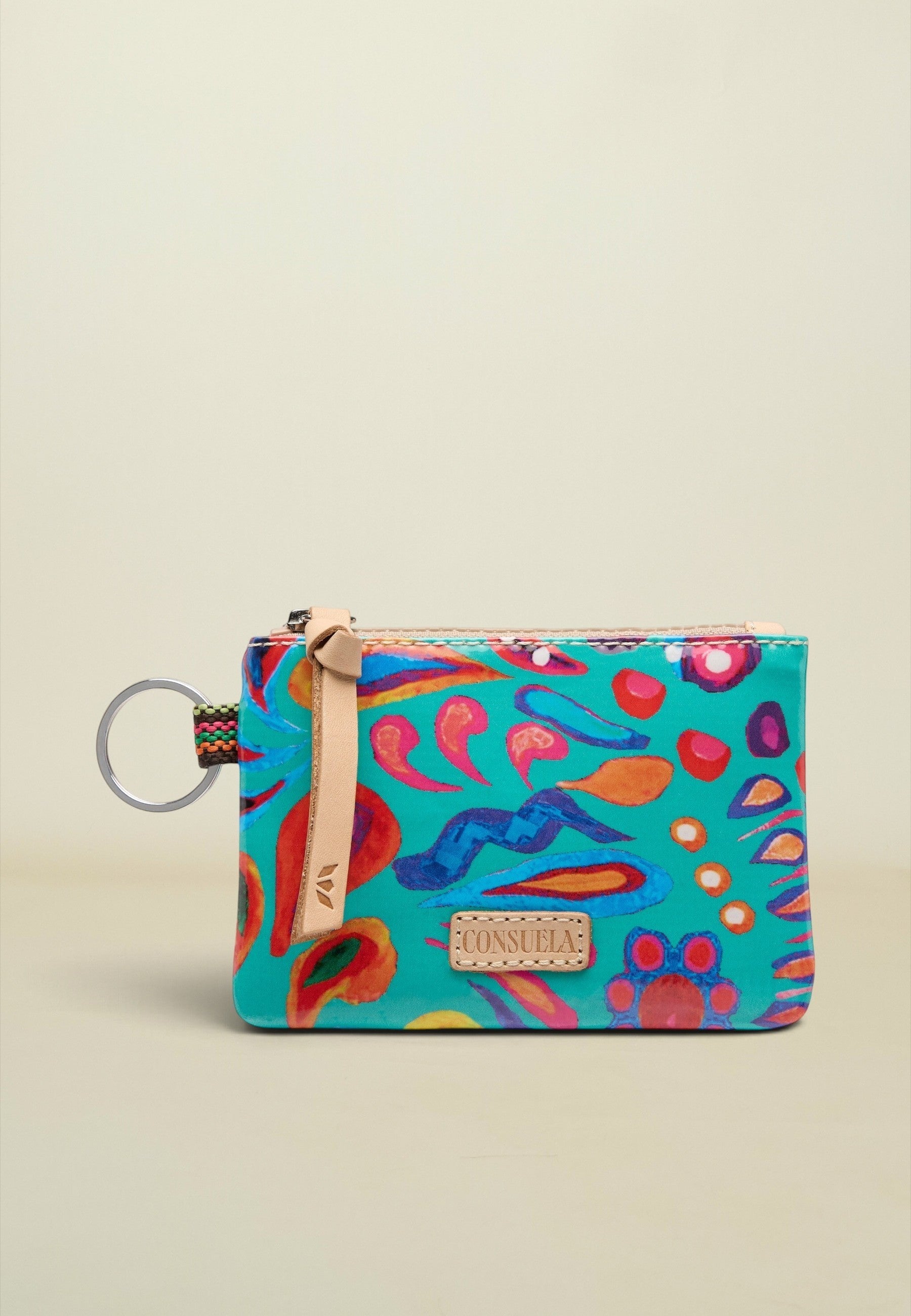 A small zippered pouch with a colorful abstract print in turquoise, pink, orange, and blue, featuring a beige leather strap and a metal key ring on a light beige background.
