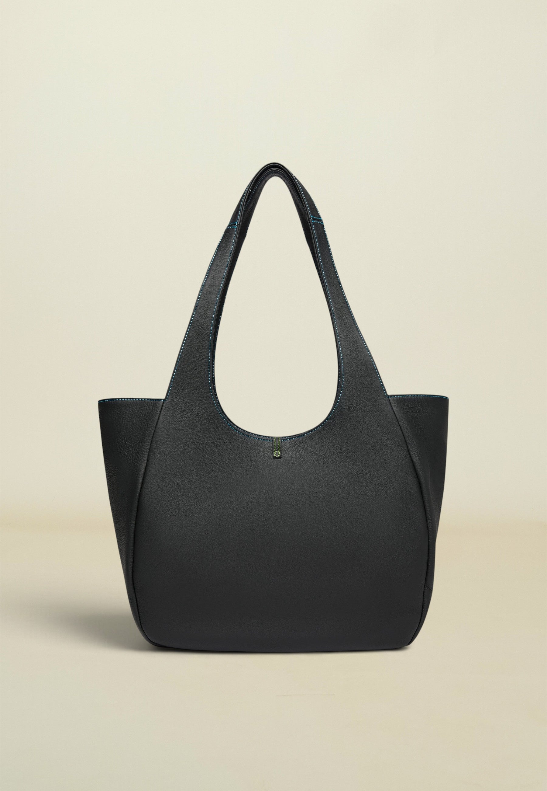 A structured black leather tote bag with a distinctive curved top handle, photographed against a solid, warm off-white background.