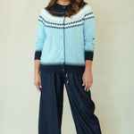A woman modeling a light blue cardigan with dark navy patterns and matching dark navy wide-leg pants, paired with brown shoes, against a plain beige background.