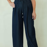 A woman modeling a sleeveless white mock-neck top and dark navy wide-leg trousers with a drawstring waist, standing against a plain light beige studio background.