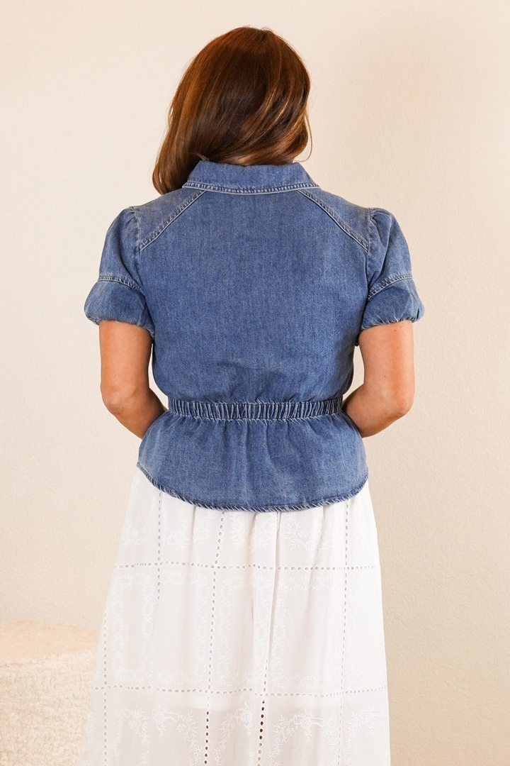 Person wearing a blue denim top over a white dress on a beige background