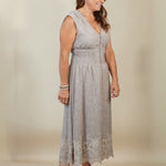 A woman modeling a sleeveless light gray midi dress with a lace hem, standing against a plain beige studio background.