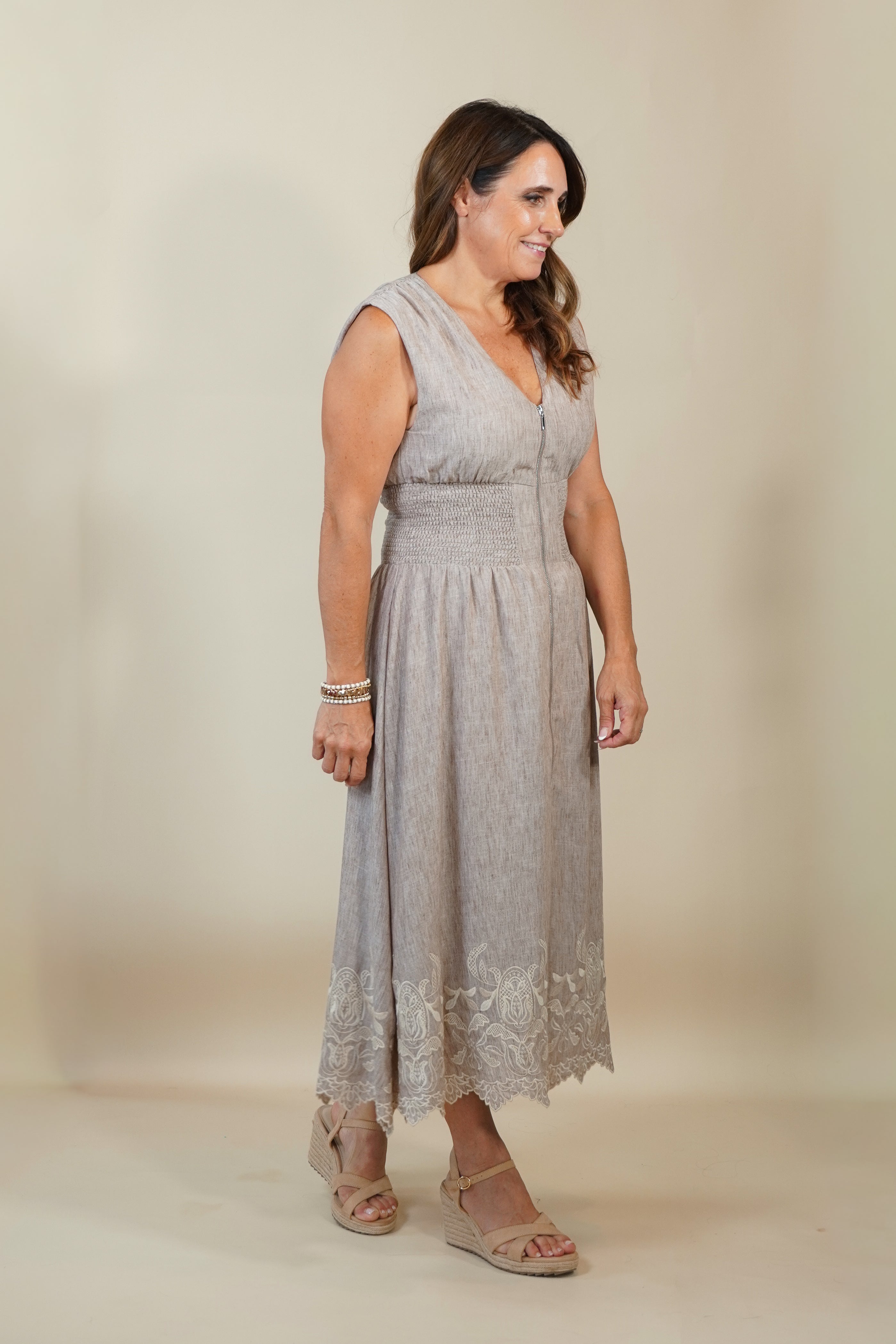 A woman modeling a sleeveless light gray midi dress with a lace hem, standing against a plain beige studio background.