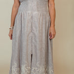 A woman wearing a sleeveless light gray midi dress with a front zipper, textured waistband, and white floral lace hem, photographed against a plain beige studio background.