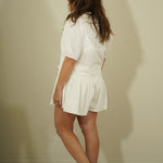 Woman wearing a white outfit against a plain wall