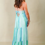 Woman wearing a long, light blue and green striped dress against a plain background