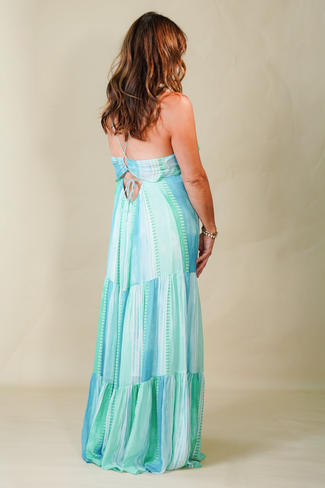 Woman wearing a long, light blue and green striped dress against a plain background