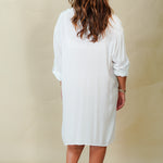 Back view woman wearing a white dress against a beige background
