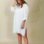 Woman wearing a white dress and sunglasses against a beige background